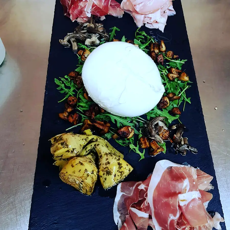 Burrata mit Rohschinken, Rucola und eingelegtem Gemüse auf der Schieferplatte